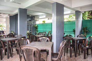 A restaurant with multiple tables and chairs, a tiled floor, and a green fence in the background. - FabHotel Ajay Inn Viman Nagar (Pune)