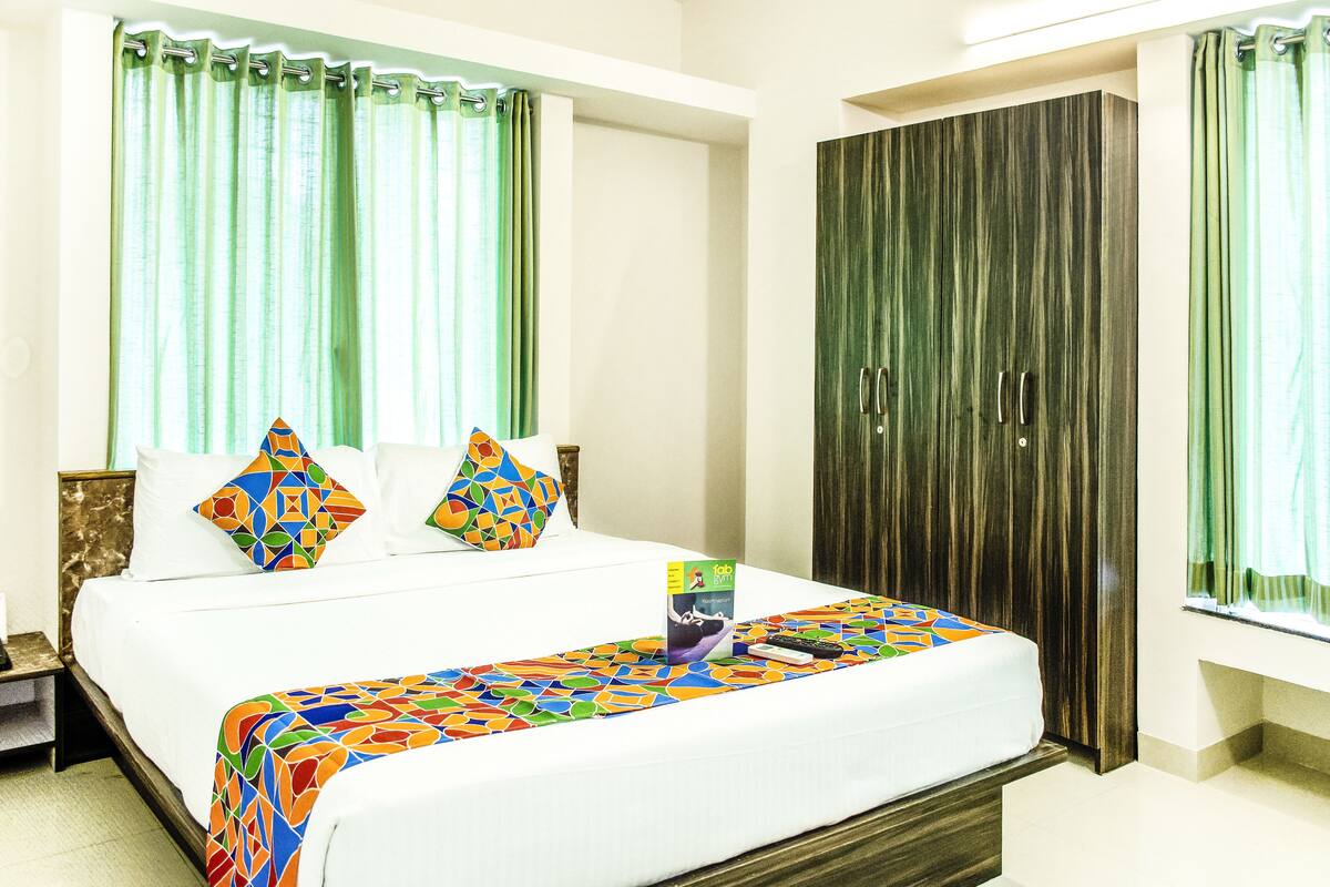 Una habitación de hotel con cama, mesita de noche, armario y cortinas verdes.