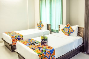 Two single beds with colorful bedspreads, a mirror, and a window with curtains.