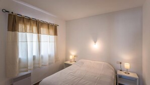 Une chambre à coucher comprenant un lit, deux tables de chevet avec des lampes, une fenêtre avec des rideaux et un luminaire fixé au mur.