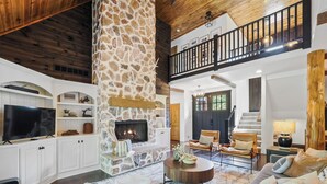 Amplia sala de estar con chimenea de piedra, techo de madera y un balcón.