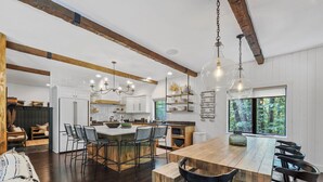 Una cocina amplia con una isla grande, vigas de madera y vistas al bosque a través de un ventanal.