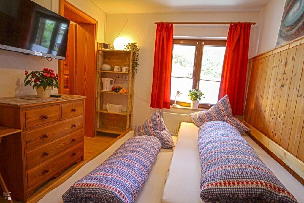 A cozy room with two beds, a wooden dresser, a TV, and a window with red curtains.