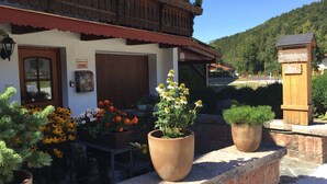 A traditional chalet with a wooden balcony, a wooden sign indicating a restaurant, and potted plants in the foreground. - Fewo Bergsteigerkammerl, 1 Person, Terrasse, 12 qm (Schönau am Königssee)