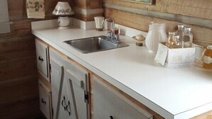 Una cocina con paredes de madera, encimera blanca, pileta y alacenas.
