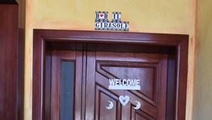 A wooden door with a 'WELCOME' sign and a 'B&B Girasole' sign above it. There are potted sunflowers to the left of the door. - Il Girasole (Assemini)