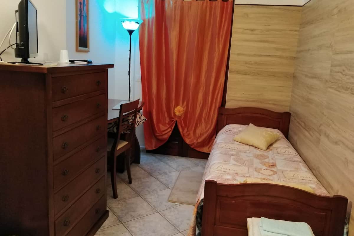 Un dormitorio con un aparador de madera, un escritorio, una silla, una cama con colcha estampada y una cortina.