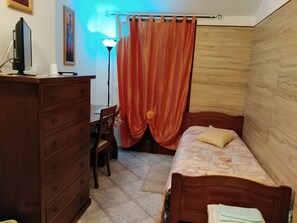 A bedroom with a wooden dresser, a desk, a chair, a bed with a patterned bedspread, and a curtain. - Il Girasole (Assemini)