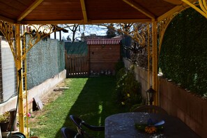 Ein überdachter Patio-Bereich mit Tisch und Stühlen, einem Holzzaun und einem kleinen Garten.