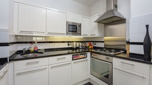A modern kitchen with white cabinets, a stainless steel range hood, a microwave, and a gas stove. - Super Central London - sleeps 4 (London)