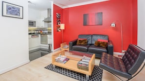 A modern living room with a red accent wall, a black leather sofa, a glass coffee table, and a black leather armchair. - Super Central London - sleeps 4 (London)