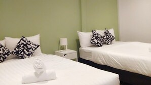 Hotellihuoneessa on kaksi sänkyä, joissa on valkoiset lakanat ja mustavalkoiset kuviolliset tyynyt. Sängyn vieressä on yöpöytä, jossa on lamppu, ja sänkyjen välissä on pieni pöytä. Seinät on maalattu vihreiksi, ja huoneen sisustus on moderni ja pelkistetty.