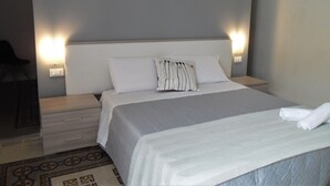 A neatly made bed with white linens and a patterned pillow, a bedside table with a lamp, and a chair in a hotel room. - Le vie del Centro (Palermo)