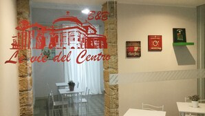 A hotel room with a stone wall, a glass door, and a view of a dining area. There are framed pictures on the wall and a sign for 'Apple Juice'. - Le vie del Centro (Palermo)