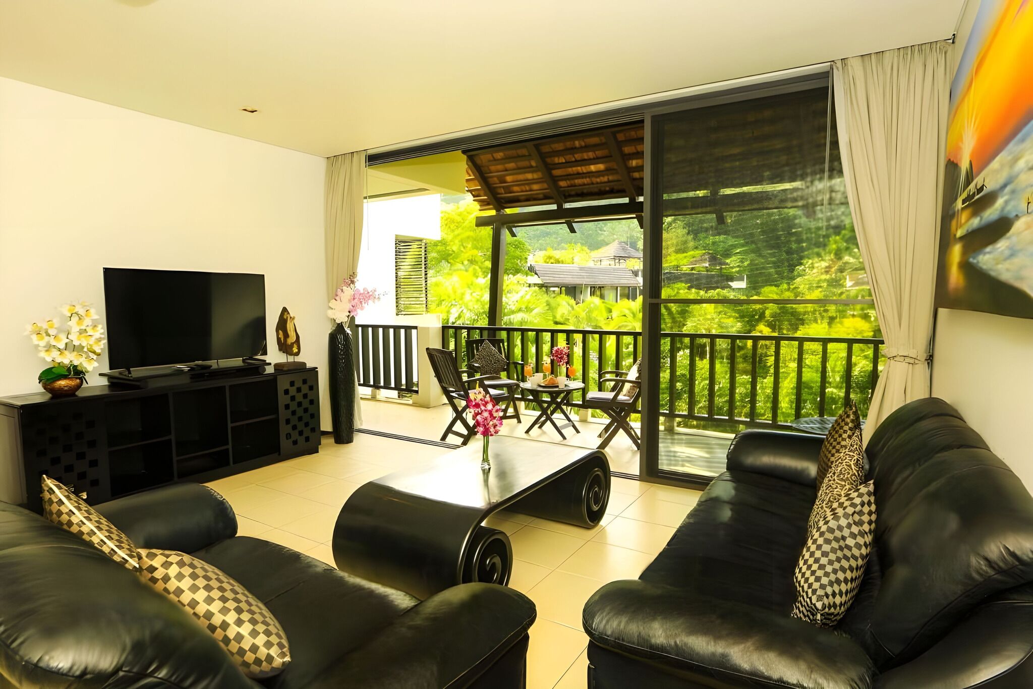 A modern living room with a flat-screen TV, black leather sofas, and a dining area with a table and chairs.
