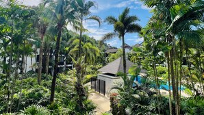 A lush tropical garden with palm trees and a building with a sloped roof. - Bangtao Beach Garden By RESAVA (Choeng Thale)
