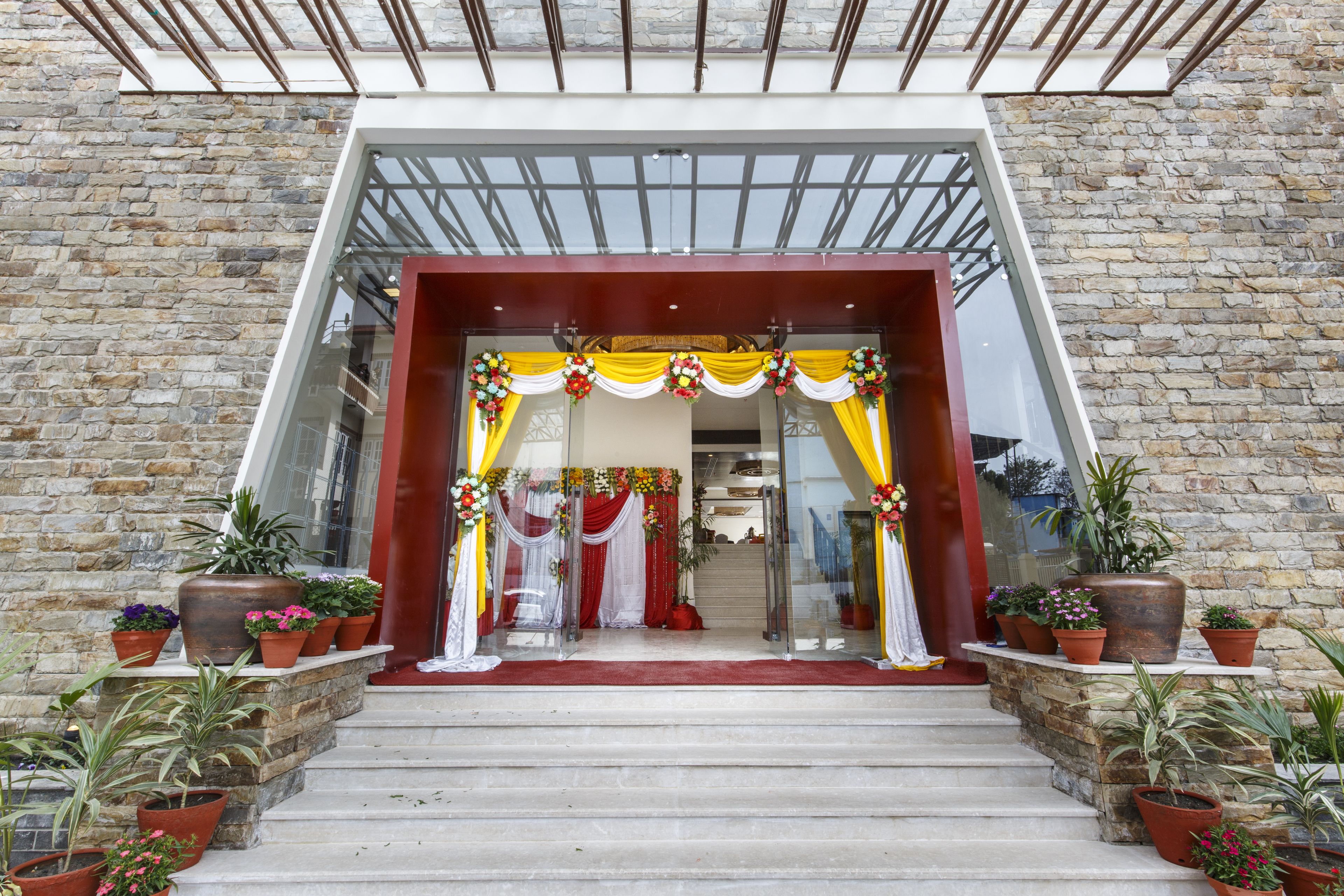 A building entrance with a stone facade, a glass door, and a red carpet leading up to a set of stairs.