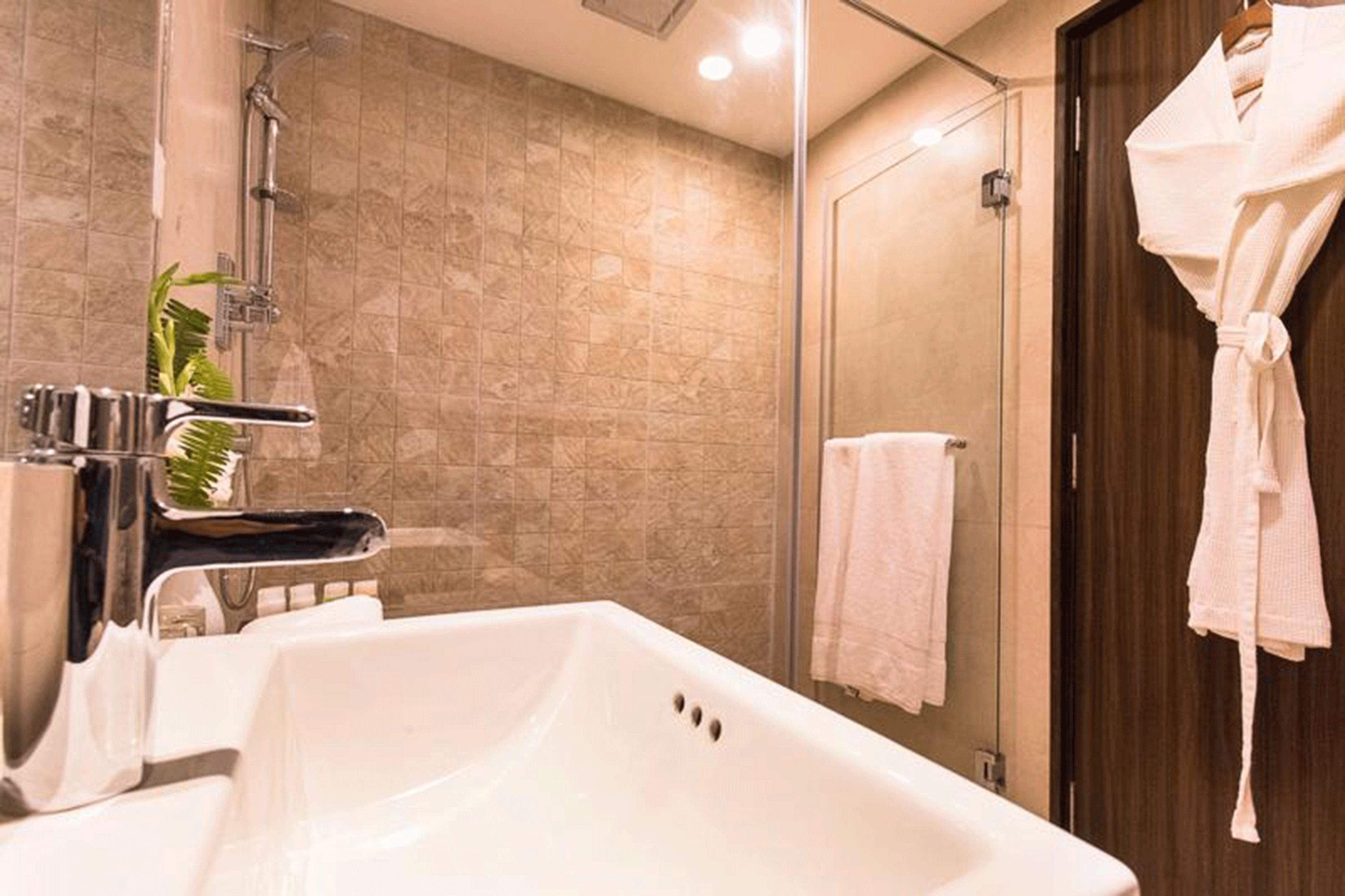 Un baño moderno con un lavamanos grande de color blanco, cabina de ducha con mampara de vidrio y puerta de madera.