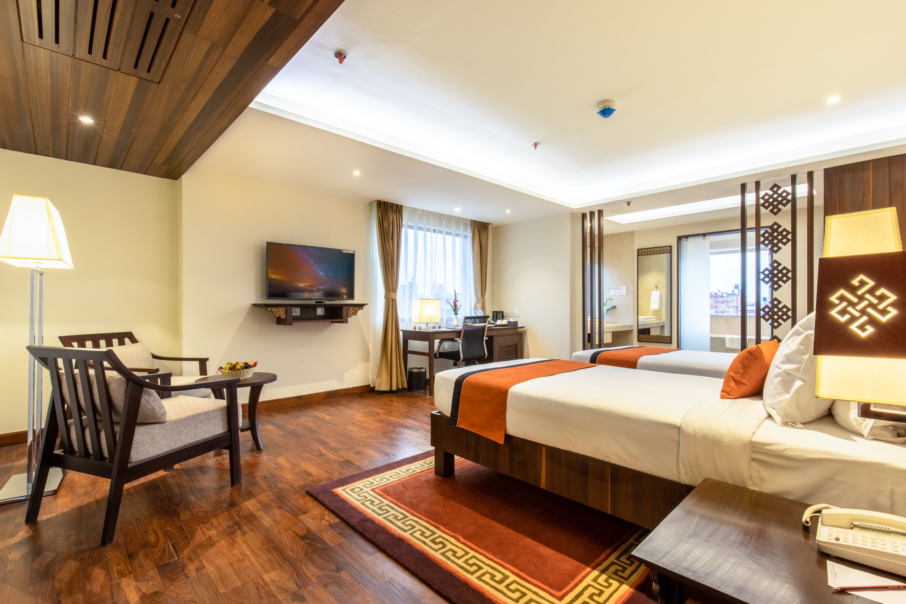 A hotel room with a bed, desk, chair, TV, and a view of the city.