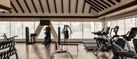 Un gimnasio con equipo de ejercicio, ventanas amplias y piso de madera.