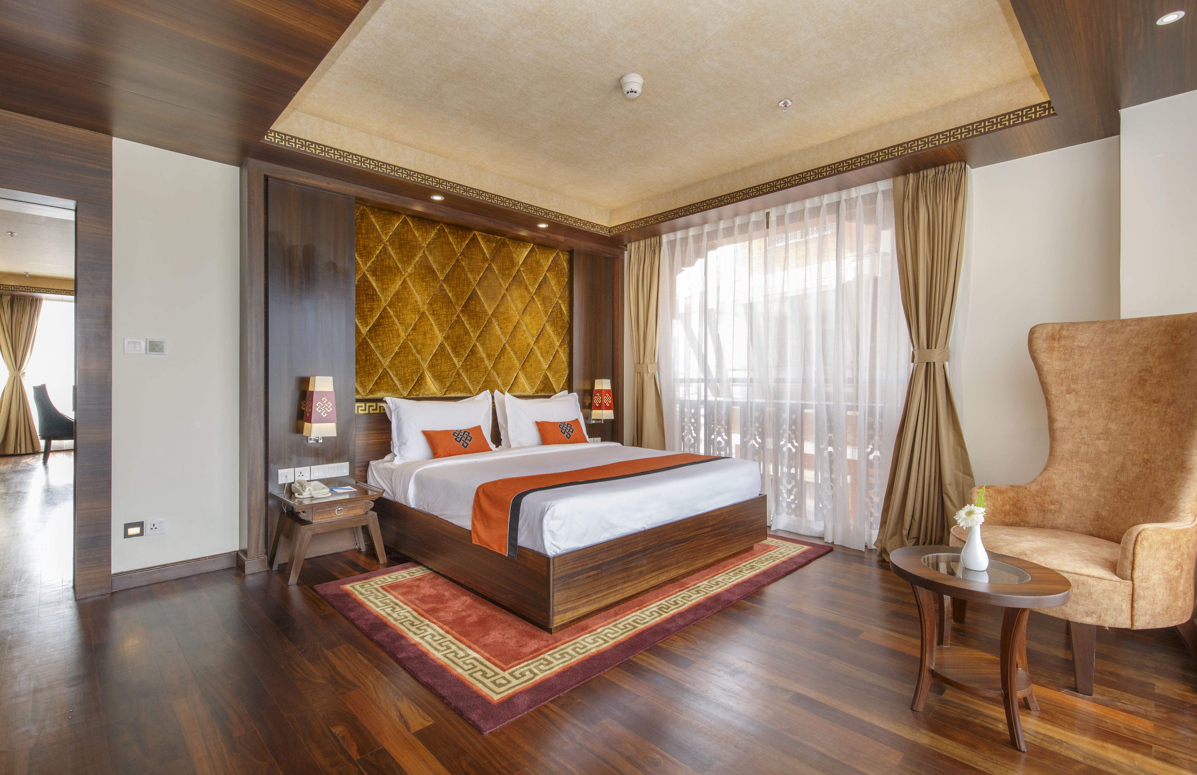 Een ruime hotelkamer met een groot bed, een zithoek met een stoel, en uitzicht op het omliggende landschap door dunne gordijnen.
