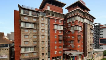 A multi-story hotel with a modern design, featuring a mix of brick and stone facades, multiple balconies, and a prominent entrance with flags.