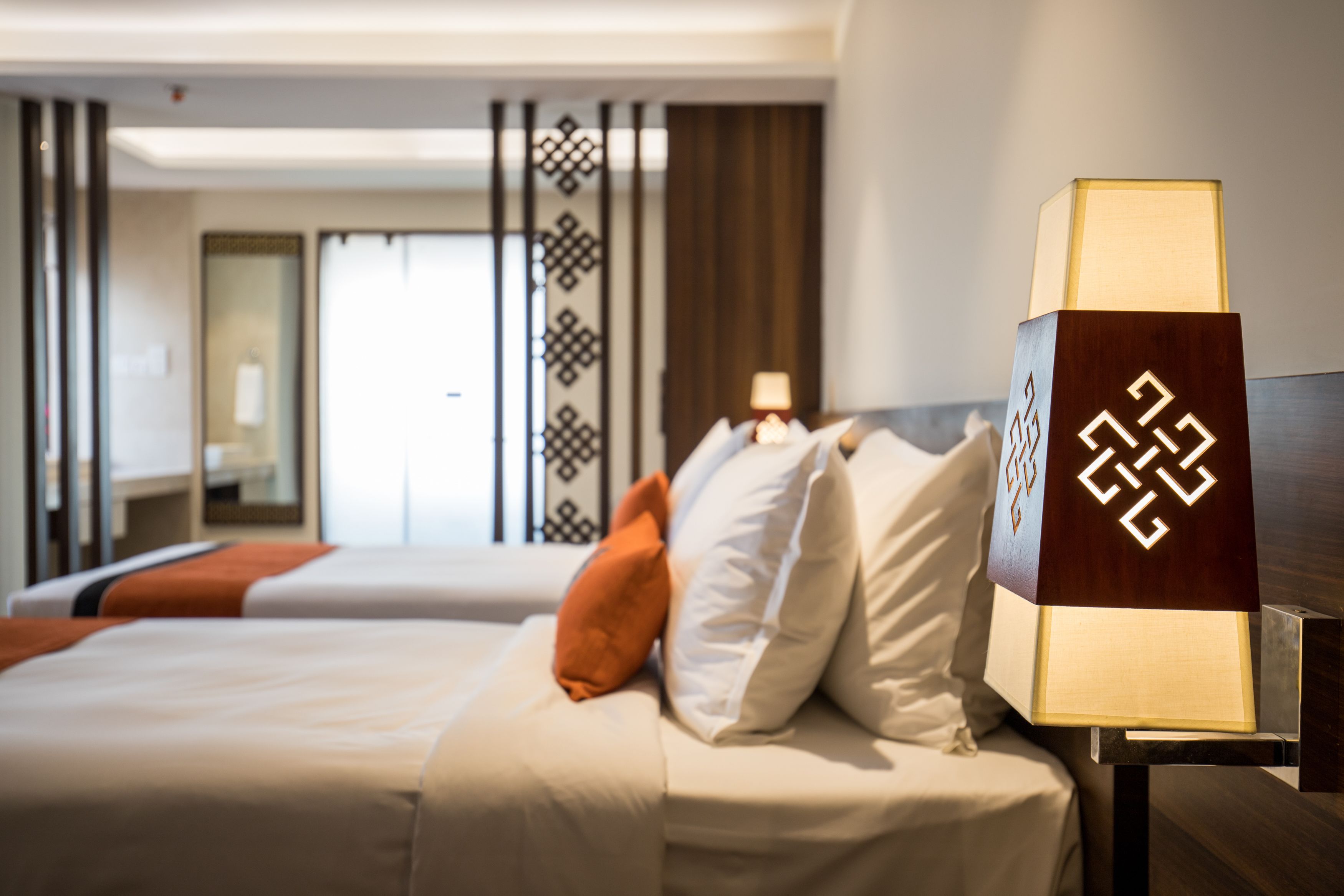 A hotel room with two beds, a nightstand with a lamp, and a decorative wall panel.