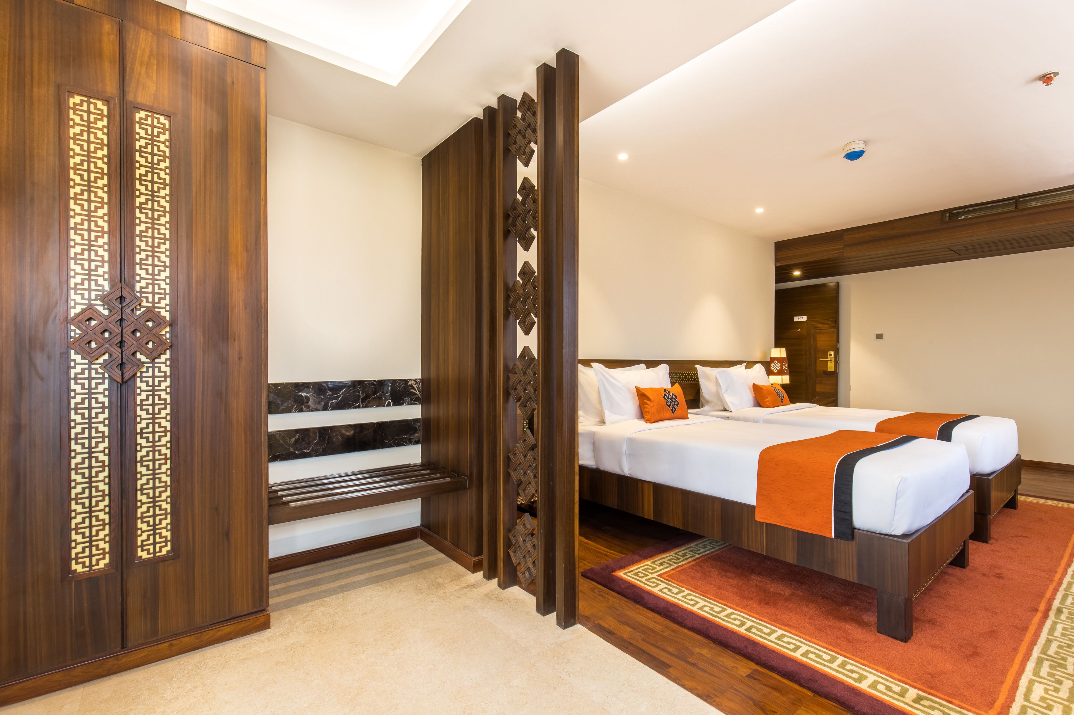 A hotel room with a large bed, a wooden wardrobe, and a bench.
