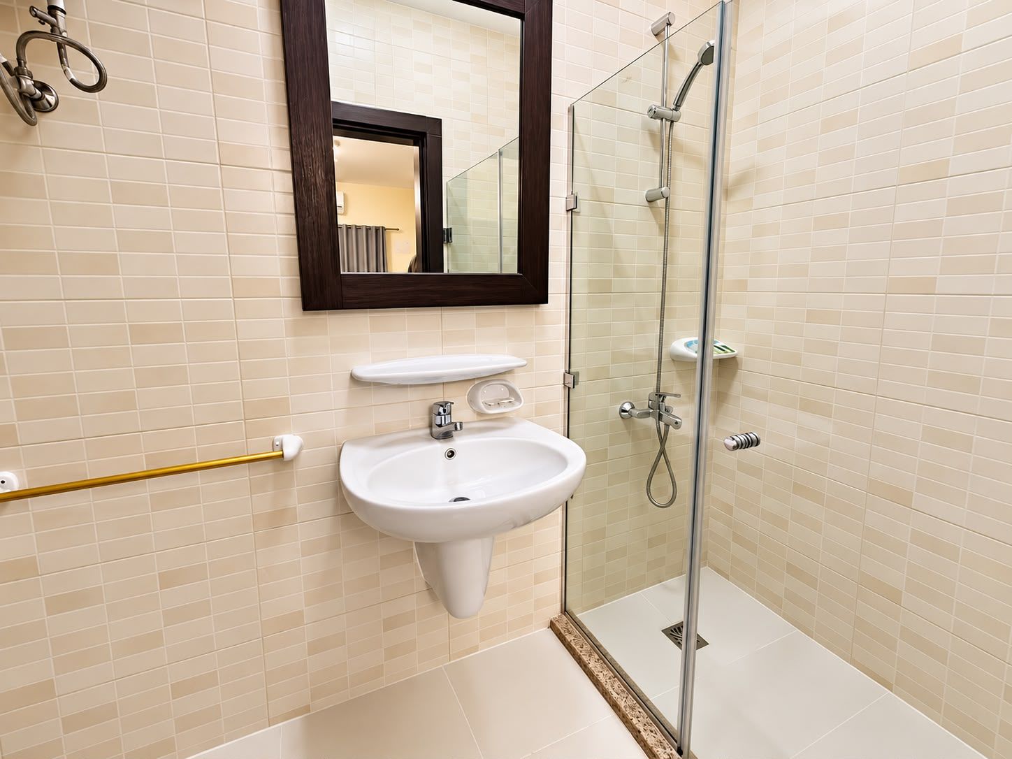Un baño con lavamanos blanco, un espejo y una ducha con mampara de vidrio.