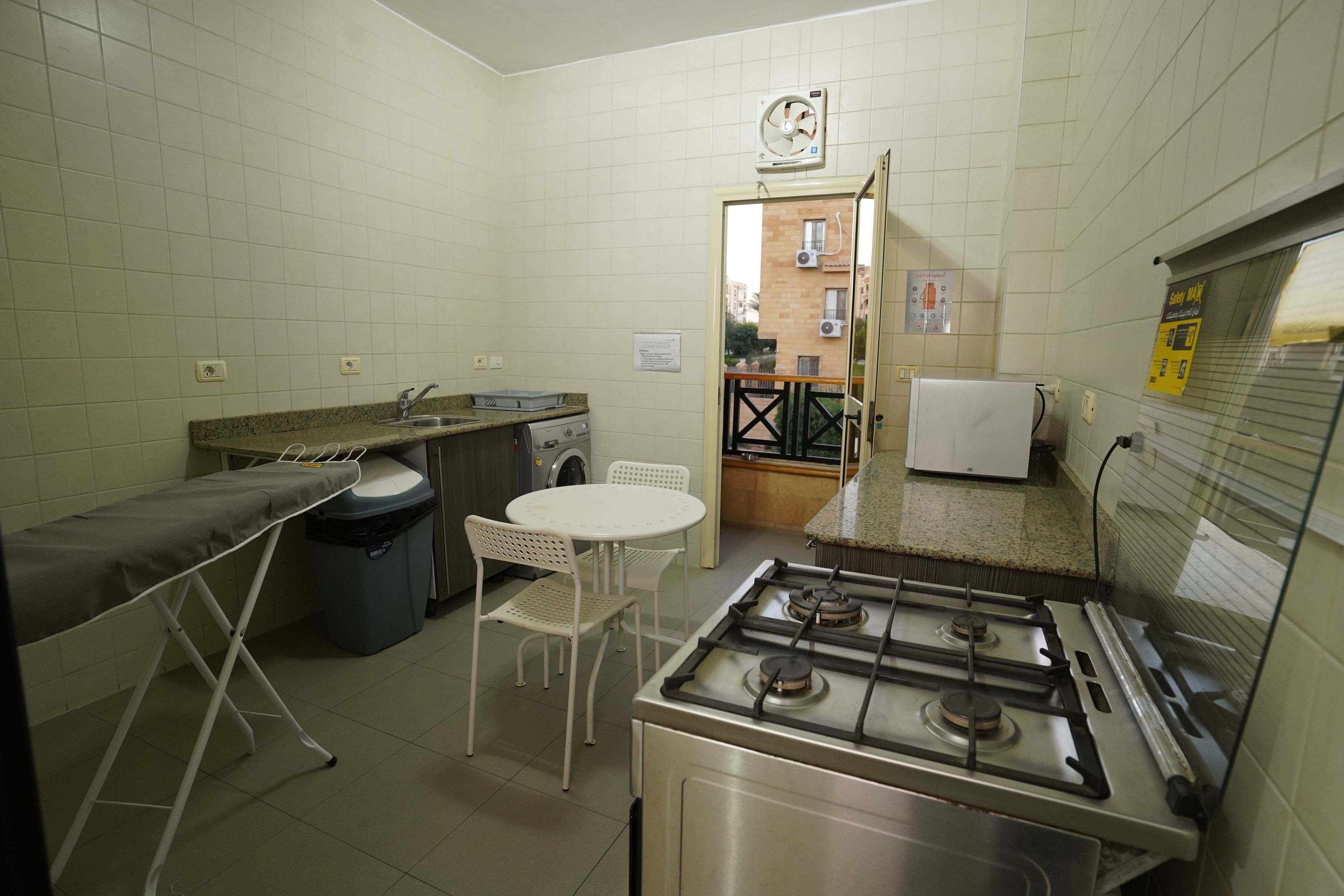 A compact kitchen with a gas stove, a sink, a small table with chairs, and a drying rack.
