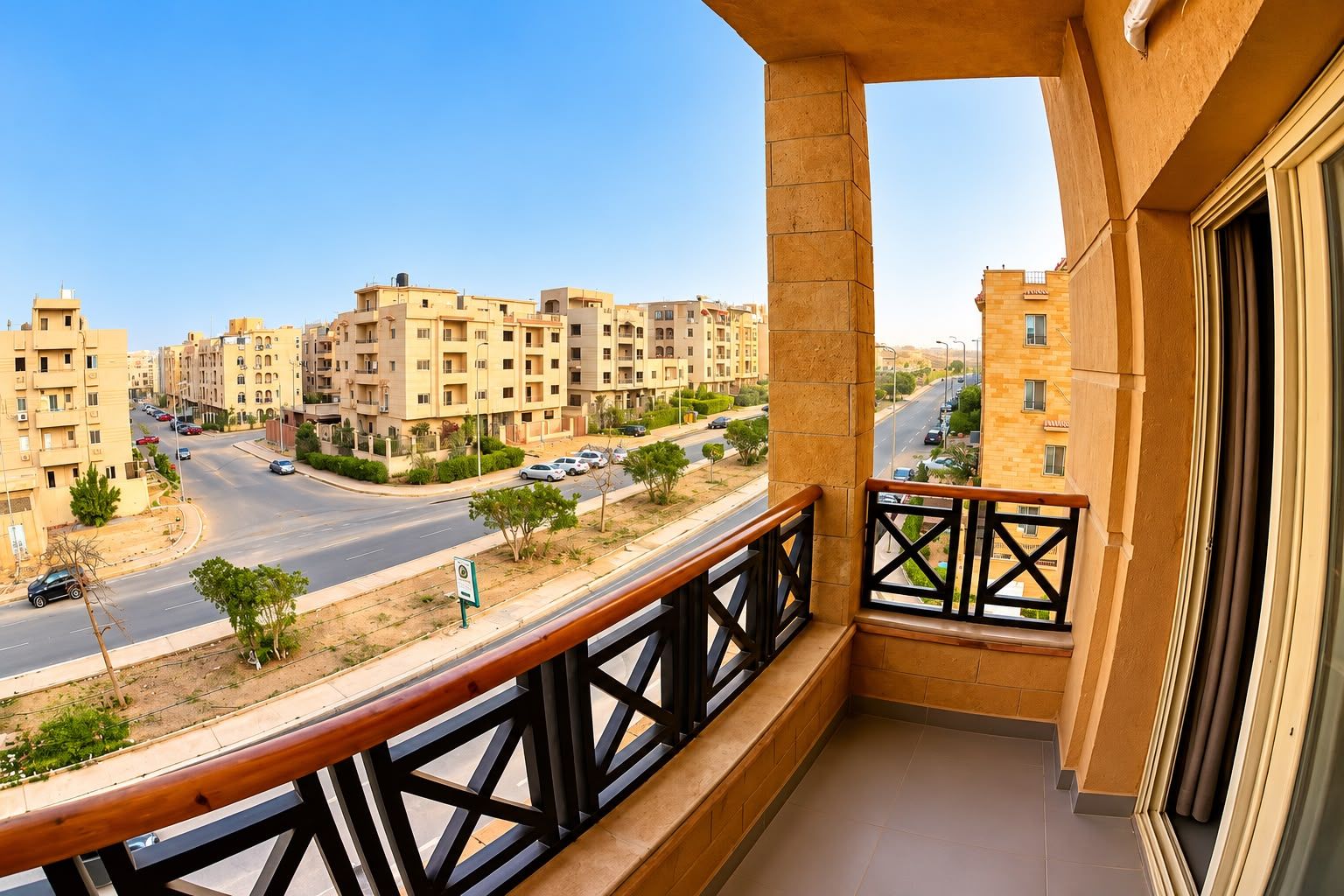 A balcony with a view of a residential area, featuring multi-story buildings and a road.