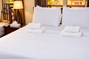 Une chambre d’hôtel avec un lit bien fait, deux oreillers, une table de chevet avec une lampe et une fenêtre donnant sur un beau paysage.