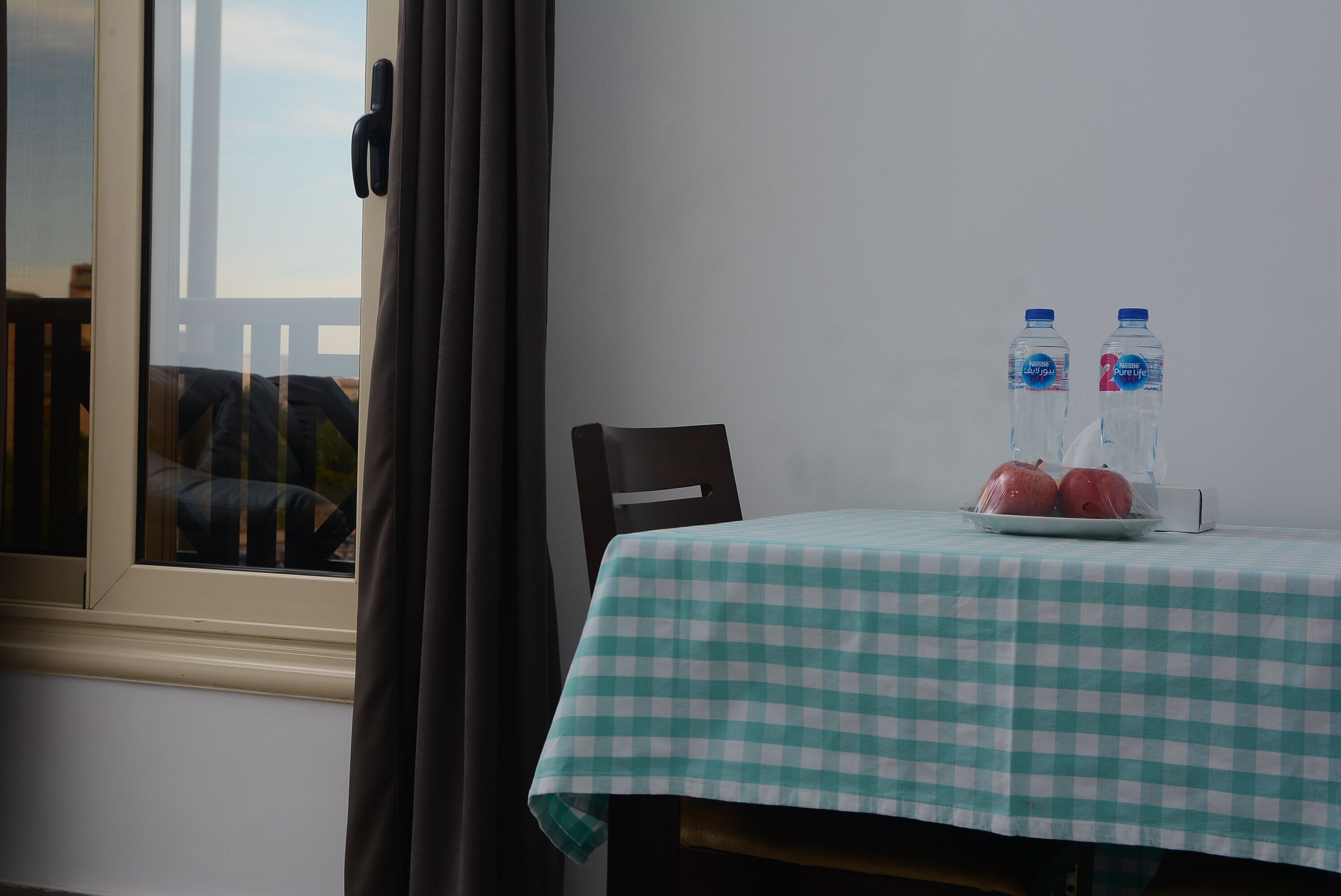 A room with a checkered tablecloth, a window with curtains, and a table with two water bottles and two apples.