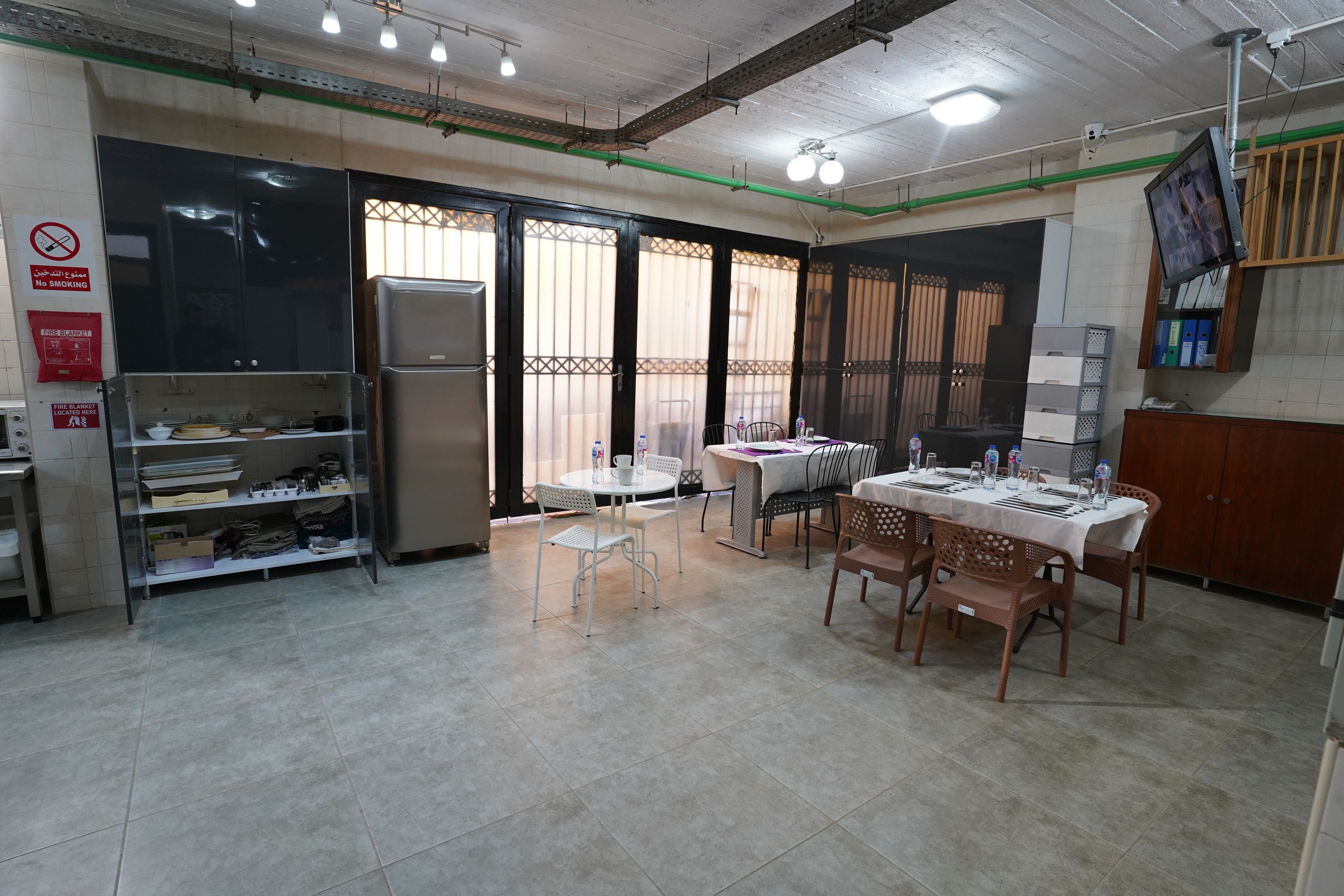 Un comedor con una mesa dispuesta para cuatro, un refrigerador y un cartel de manta ignífuga en la pared.