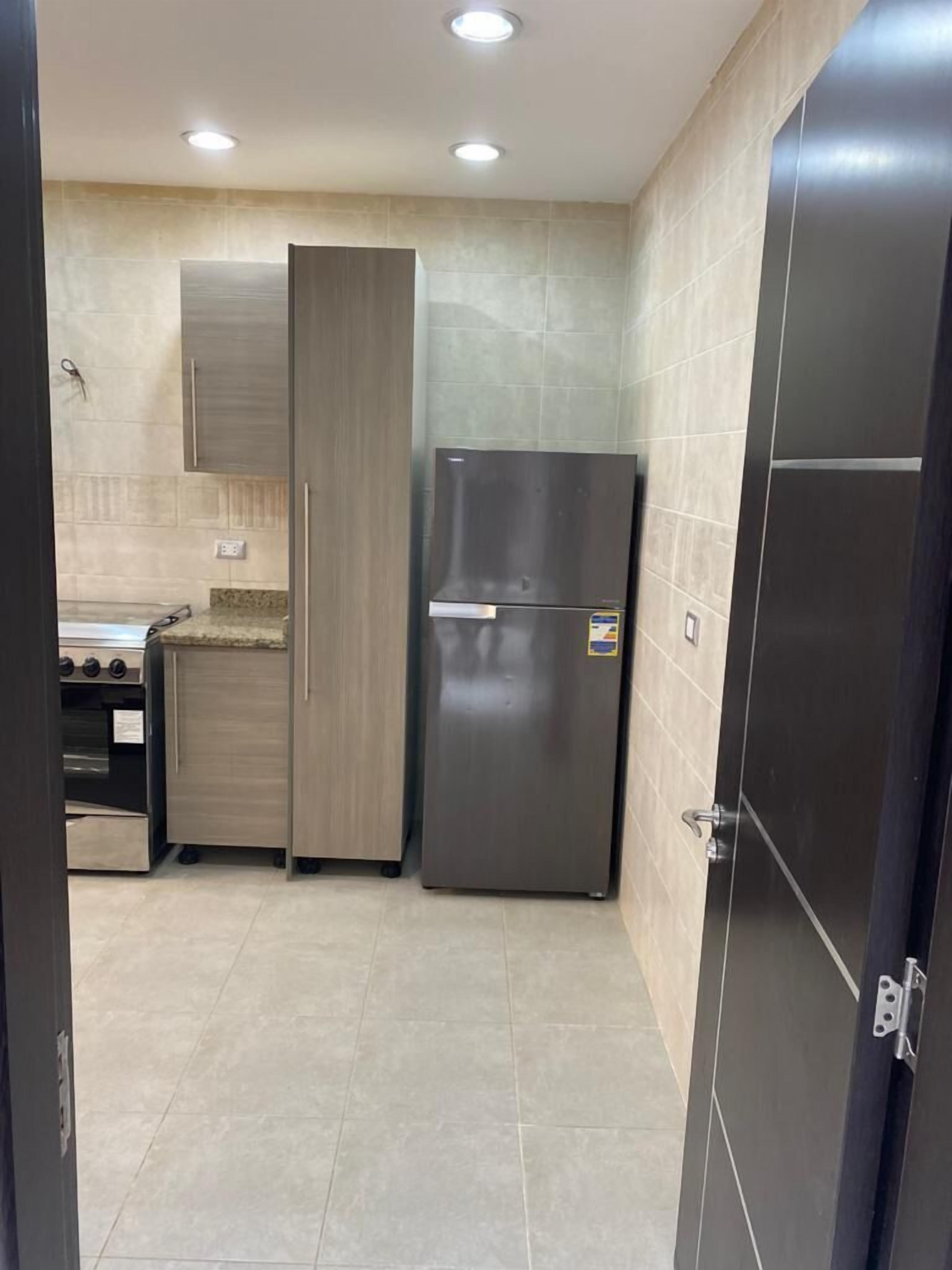 A compact kitchen with a built-in oven, a stainless steel refrigerator, and light-colored tiled flooring.