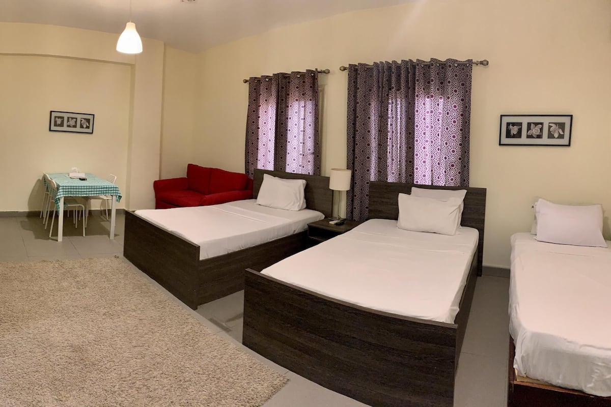 A hotel room with two beds, a small table with a chair, a refrigerator, and a phone on the wall.