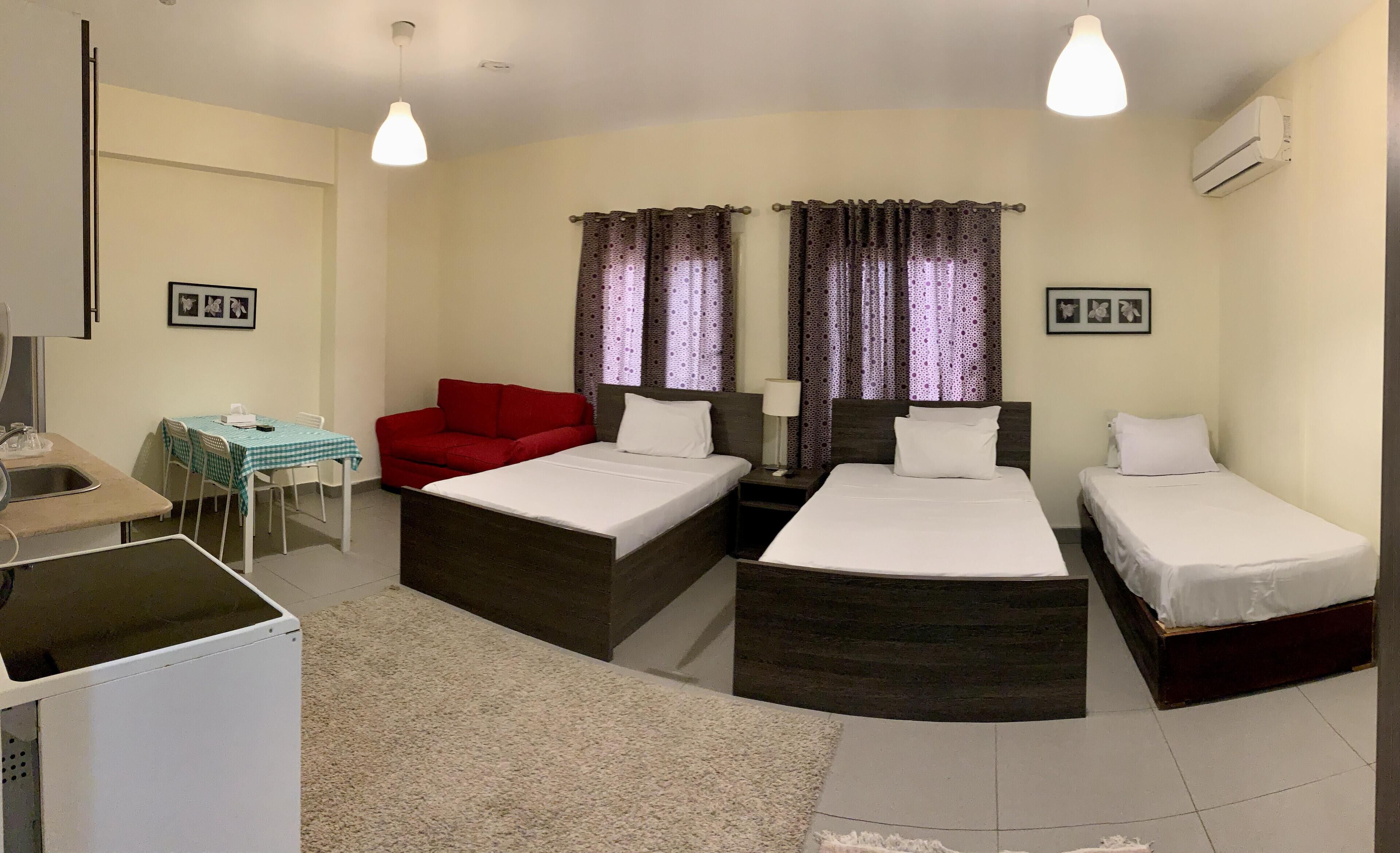 A hotel room with two beds, a desk, a chair, a red sofa, and curtains.