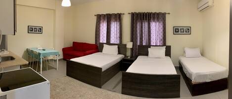 A hotel room with two beds, a desk, a chair, a red sofa, and curtains.