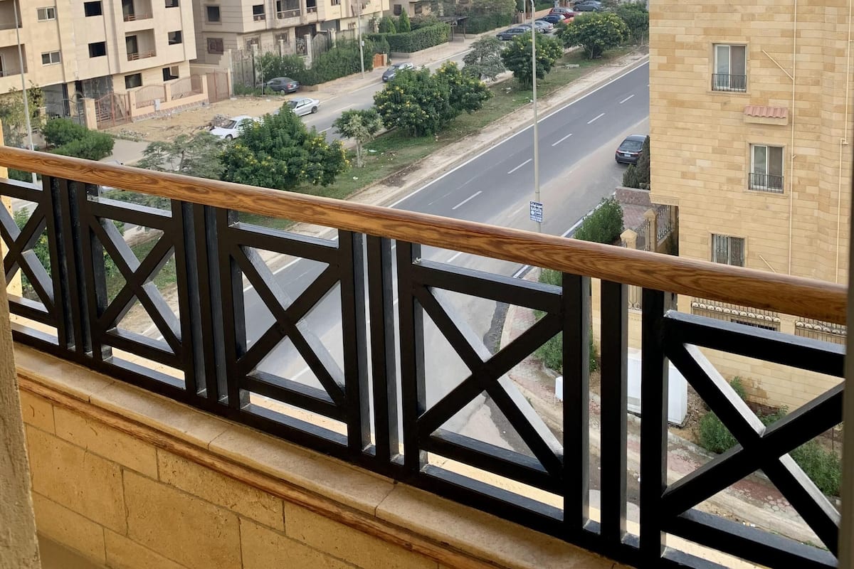 A residential area with multi-story buildings, a clear road, and a balcony with a wooden railing.