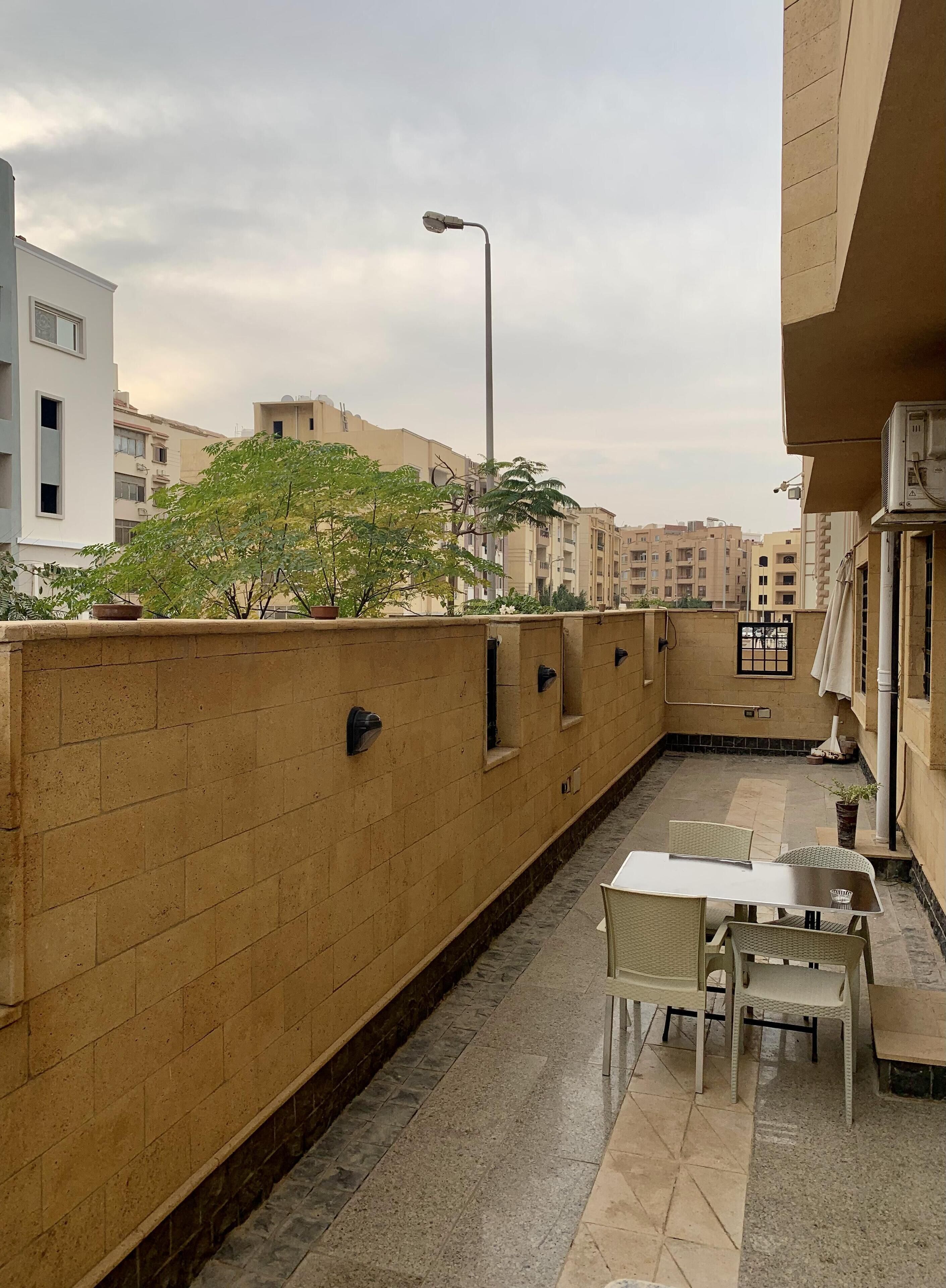 A rooftop patio with a table and chairs, a street lamp, and a view of surrounding buildings.