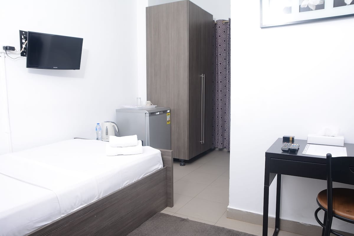 A hotel room with a bed, a desk, a wardrobe, a television, and a shower area.