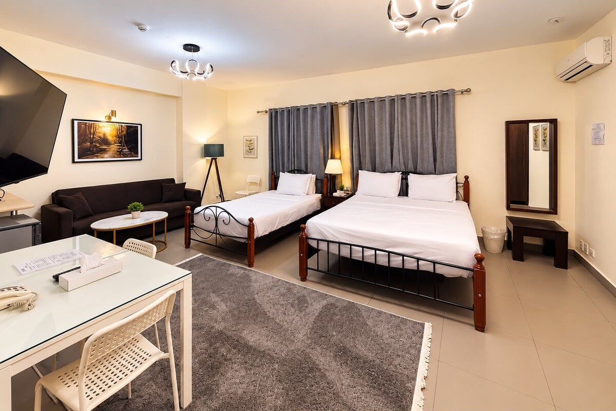 A hotel room with a bed, a desk, a chair, a sofa, a lamp, and a television.