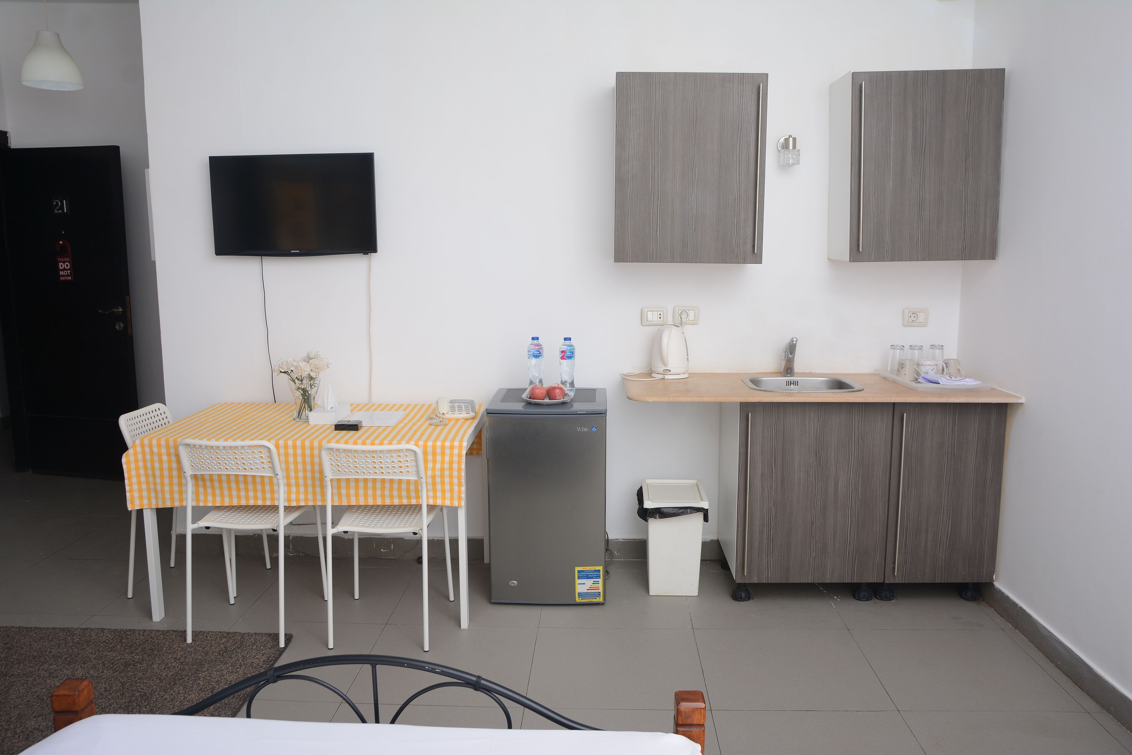 Una habitación de hotel compacta con una mesa de comedor, sillas, una pequeña cocina, un televisor y un armario.