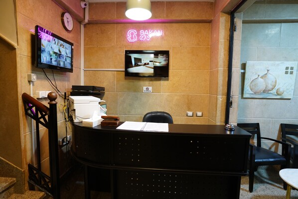 A hotel reception area with a reception desk, a clock, a television displaying a room, and a 'No Smoking' sign. - Sakan 275 (New Cairo)