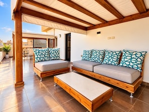 A covered outdoor seating area with a sofa and a coffee table, wooden beams, and a tiled floor. - Sakan 275 (New Cairo)