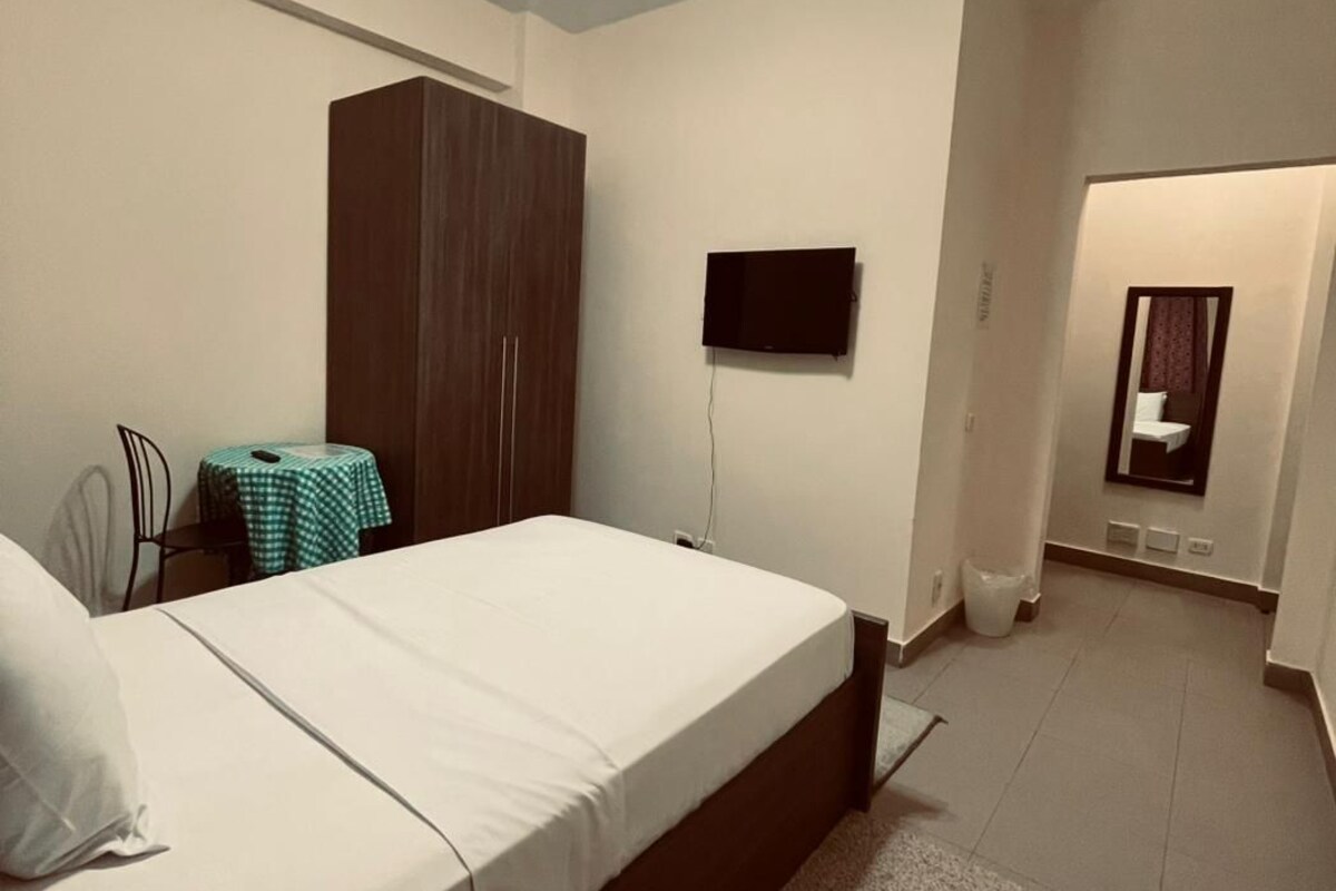A bedroom with a bed, a wardrobe, a television, and a small table with a chair.