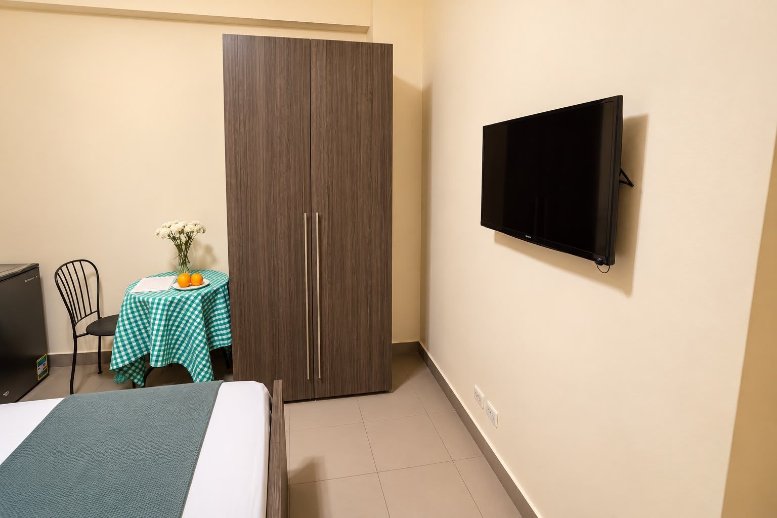 A room with a bed, a wardrobe, a desk with a table, and a television mounted on the wall.