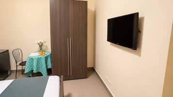 Una habitación con una cama, un armario, un escritorio con mesa y un televisor montado en la pared.