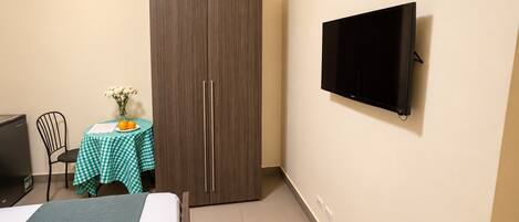 A room with a bed, a wardrobe, a desk with a table, and a television mounted on the wall.