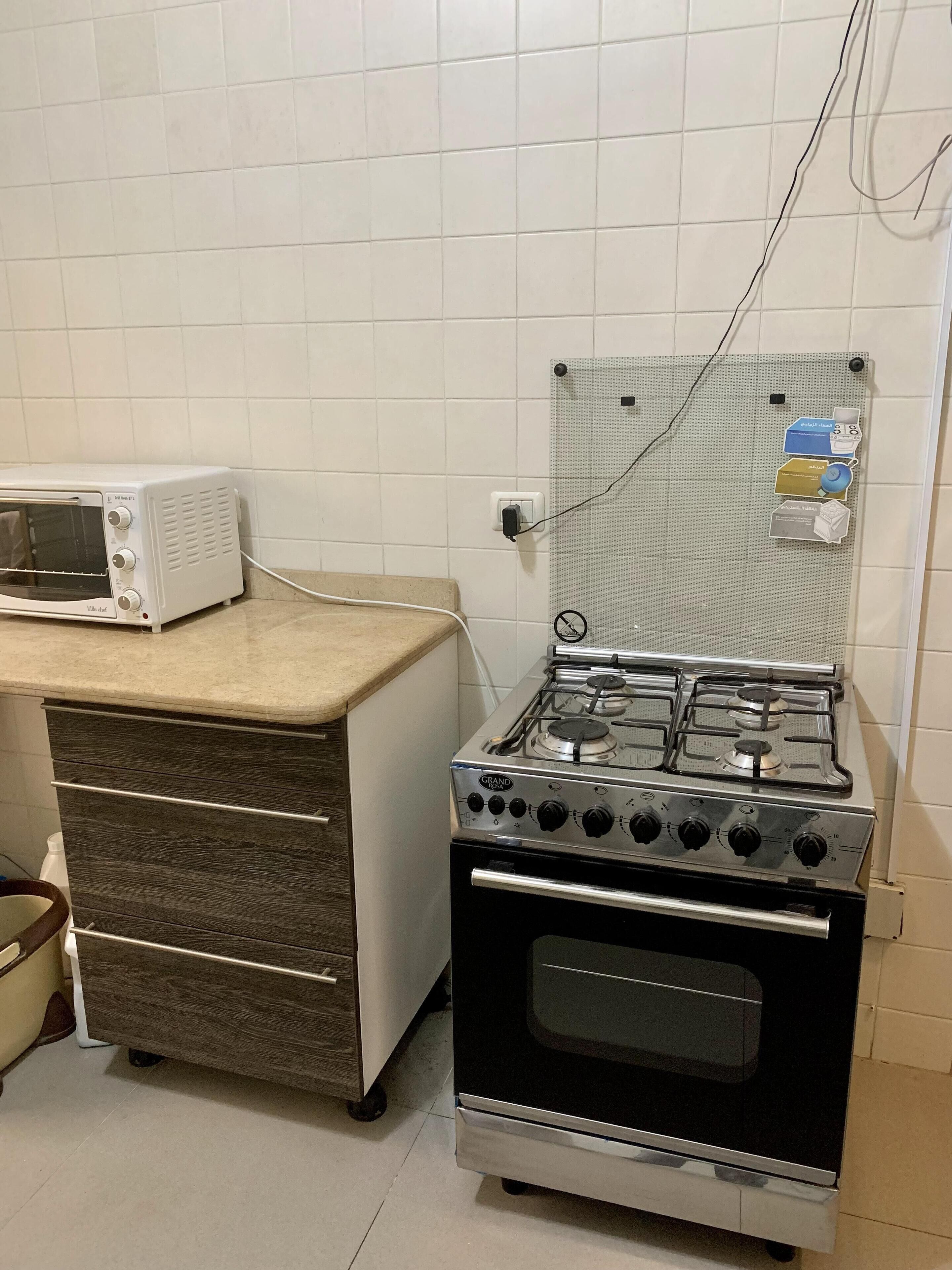 A kitchen with a white tiled backsplash, a white toaster oven, a stainless steel gas stove, and a wooden drawer unit.